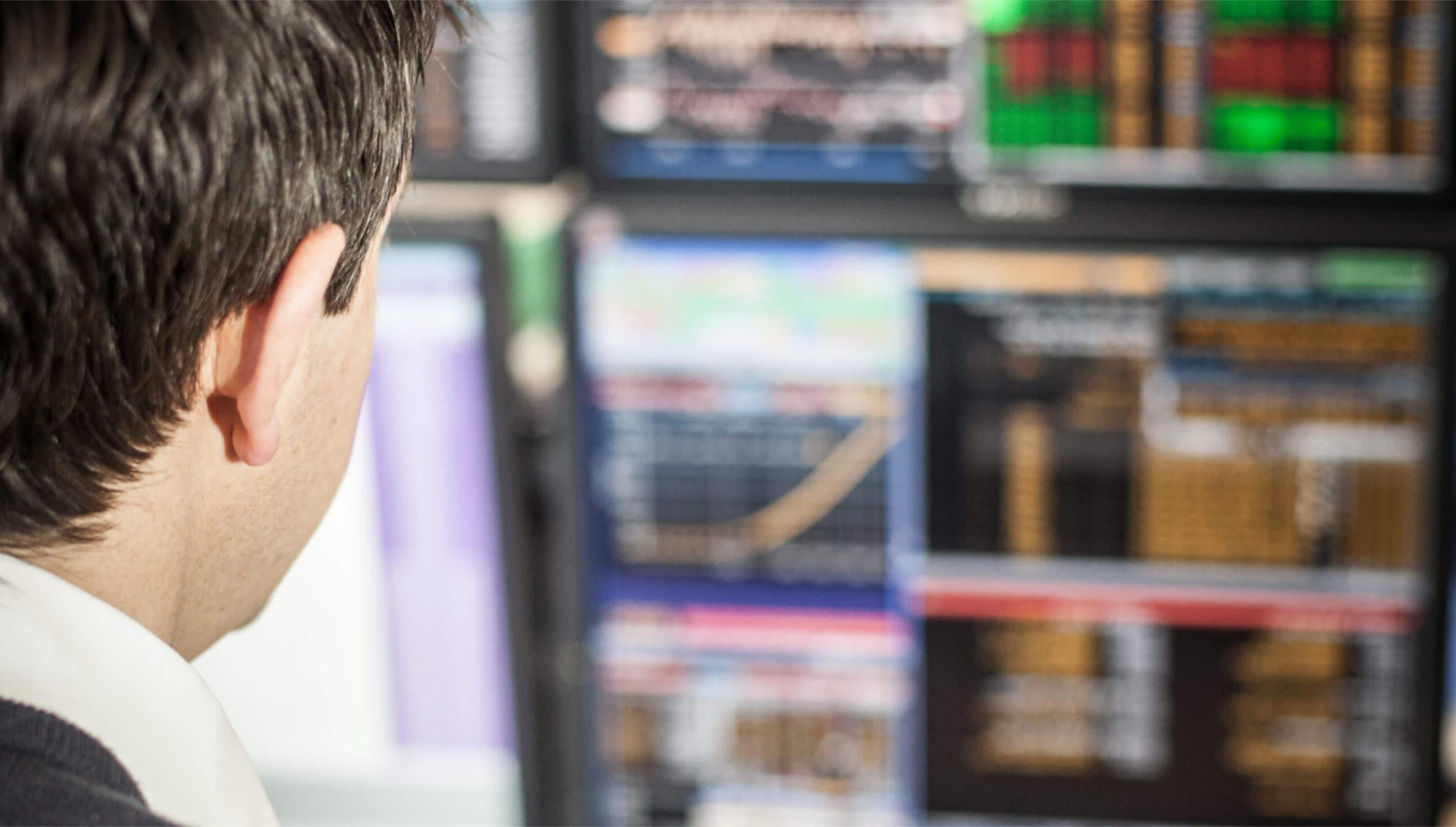 Close up behind a man looking at various computer screens showing data